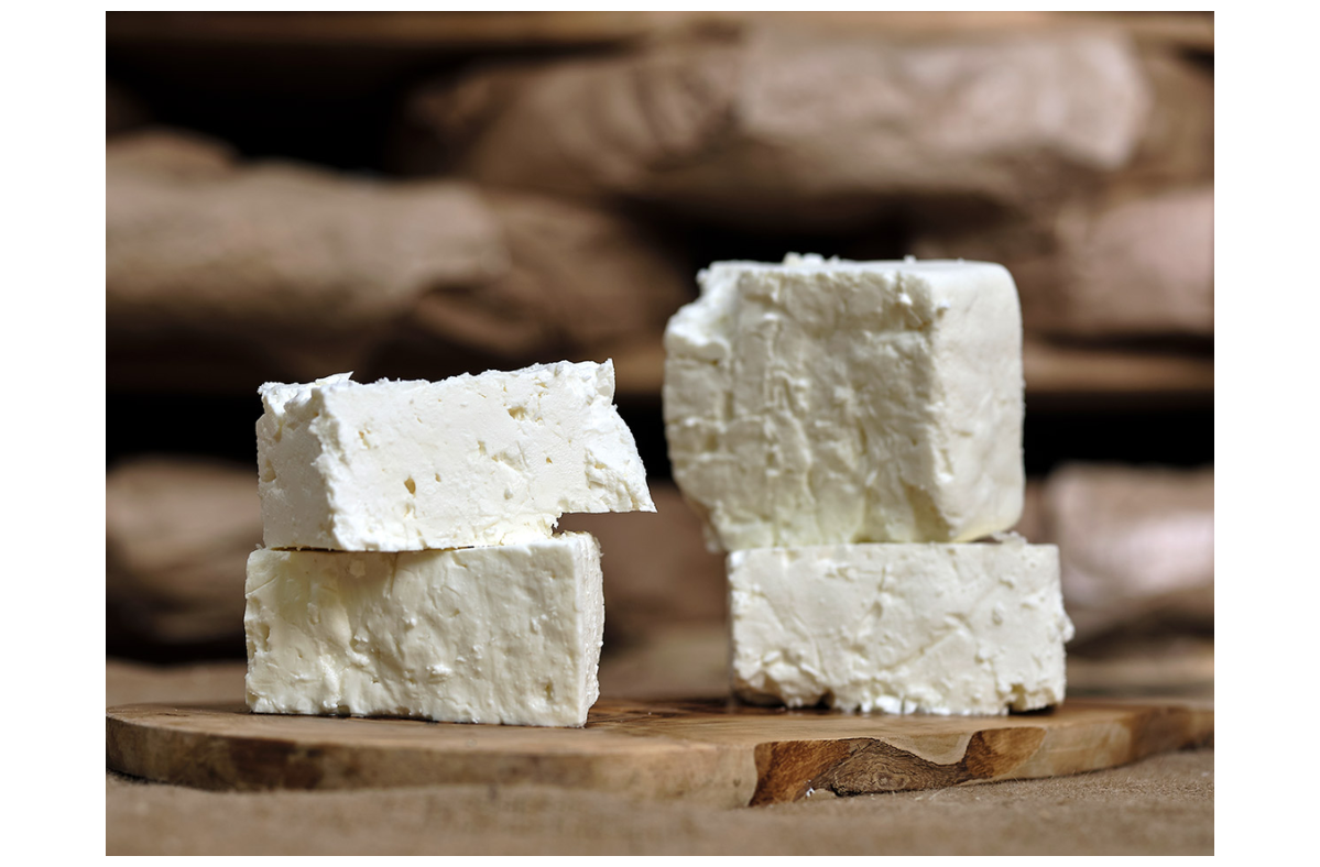 Blocks of feta cheese stacked on a wooden serving board against a rustic stone background.